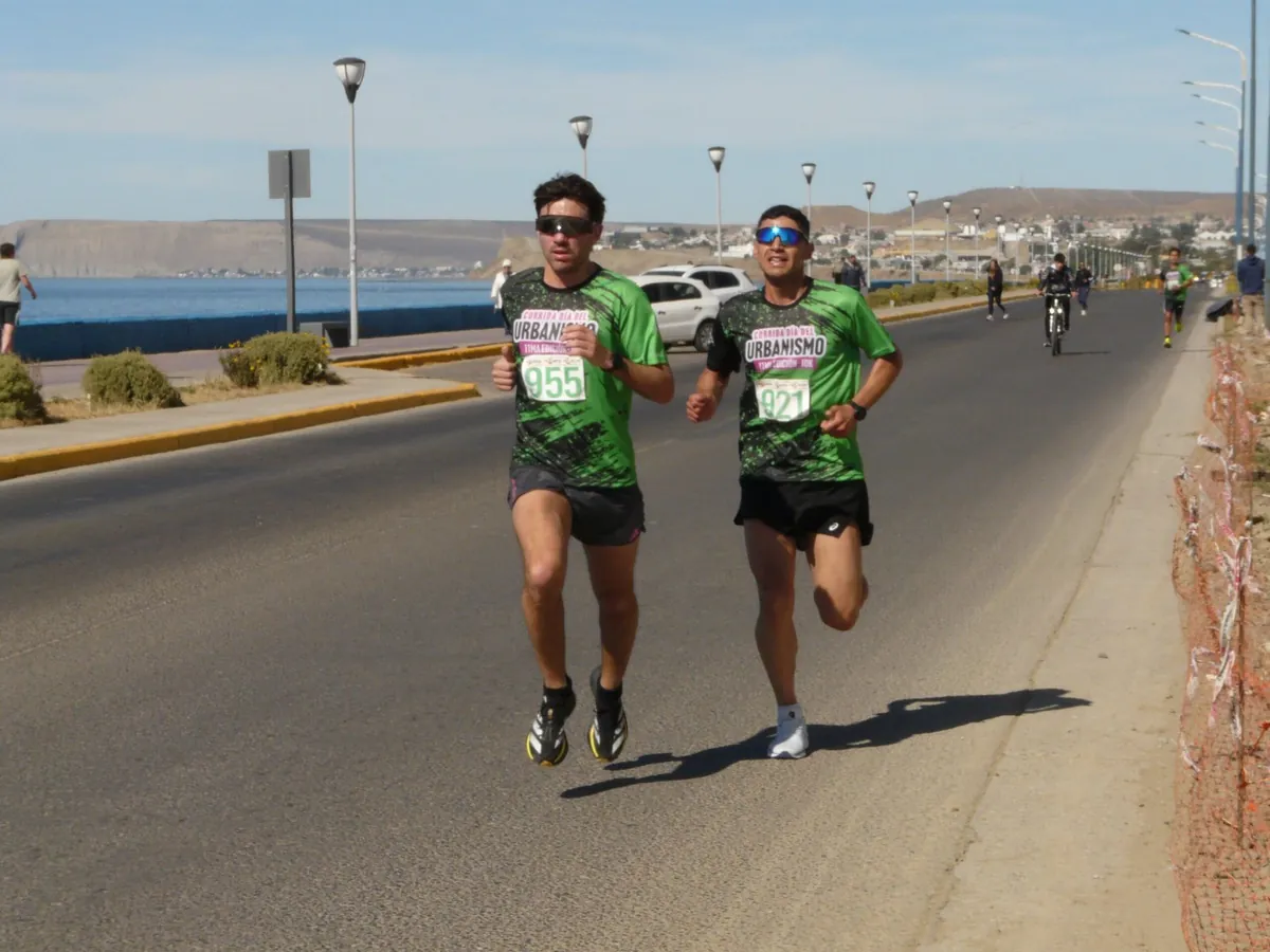 Dos corredores con remeras verdes sublimadas de la Corrida Día del Urbanismo sobre la costanera